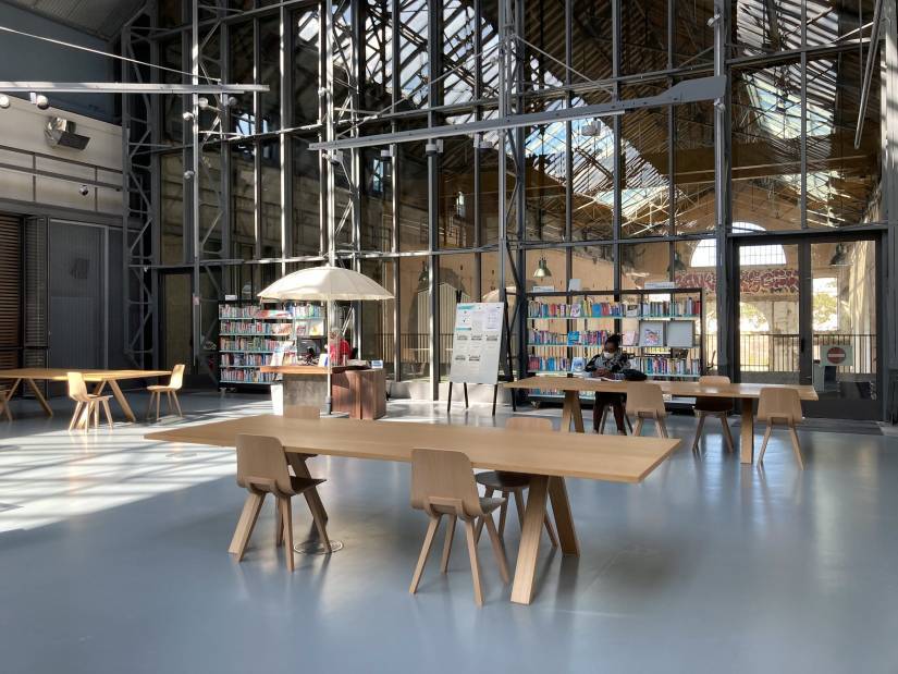 photo de la médiathèque des capucins avec une table au premier plan et des etals de livre au second, dans un grand atelier industriel